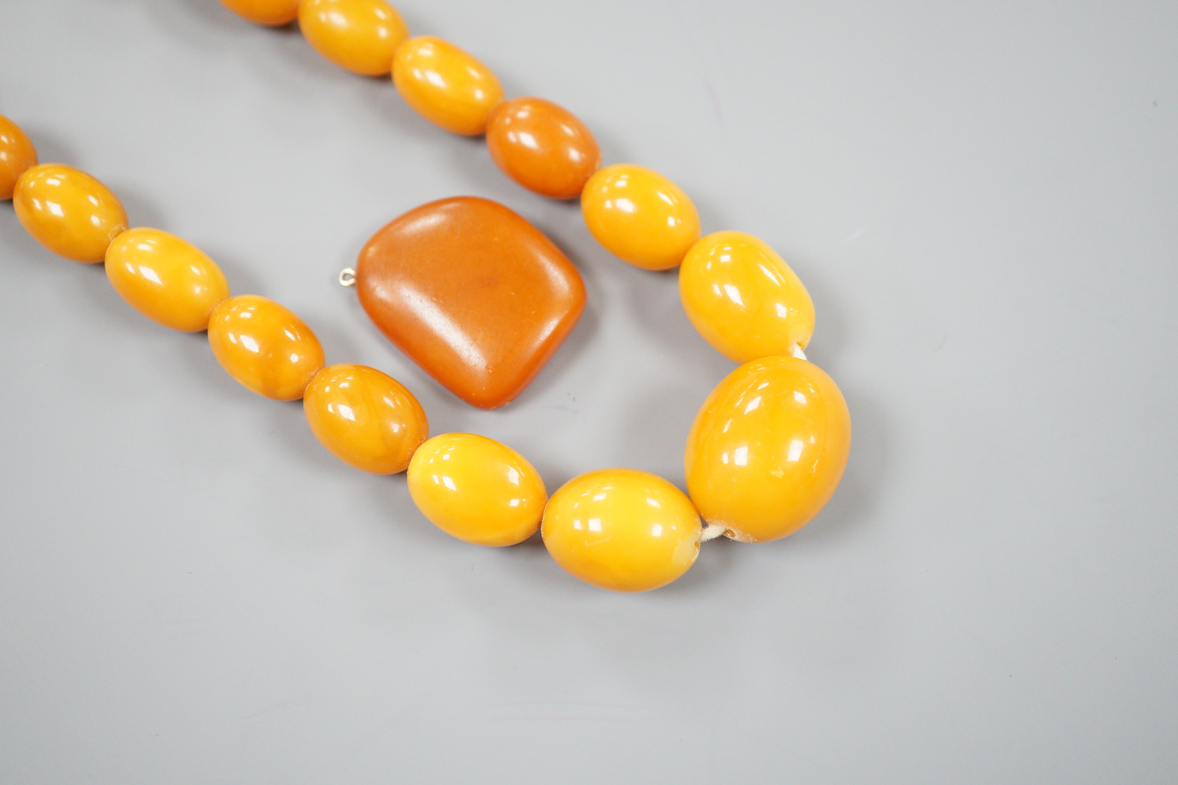 A single strand graduated oval amber bead necklace, 70cm, gross weight 64 grams, together with an amber pebble pendant, gross 5 grams.